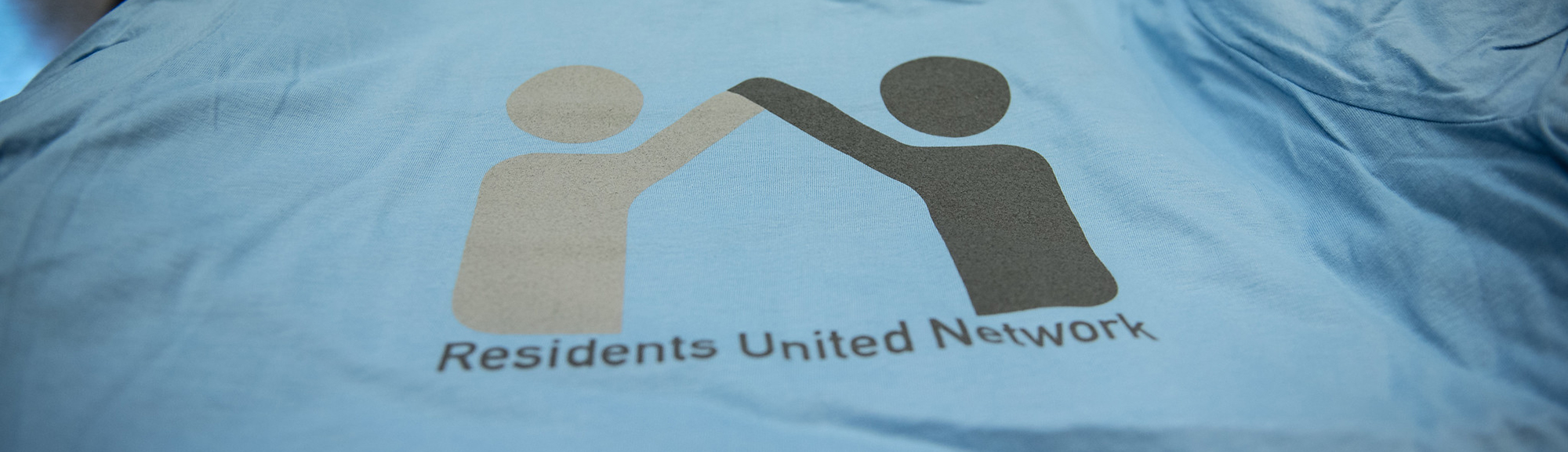 A close-up of a light blue t-shirt with Residents United Network printed on the front.