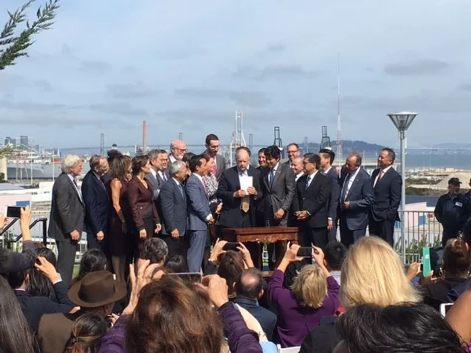 A group of Housing California supporters stands on a raised platform in San Francisco by the water, in front of a crowd. Governor Jerry Brown is on the center of the group, and Housing California Executive Director, Lisa Hershey, is also on the stage. The crowd are taking photographs with their smartphones. 