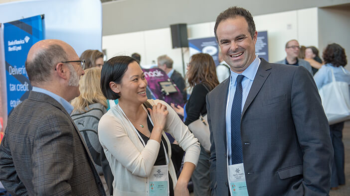 Three attendees at the Housing California Annual Conference stand amid the supporter booths, laughing and enjoying their time together.