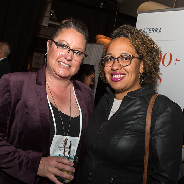 Two women, both smiling and wearing glasses, attend the evening mixer at the Housing California Annual Conference.